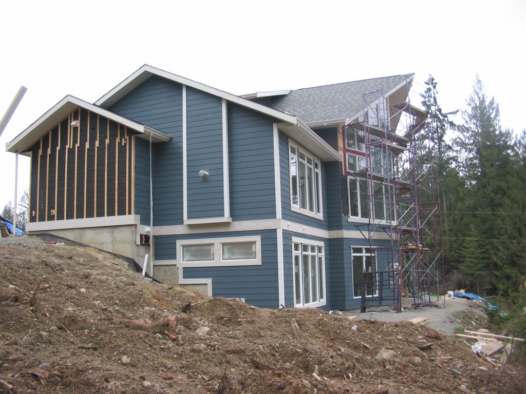 Building exterior under construction with siding, windows, roofing, and scaffolding